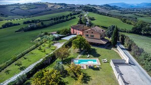 An aerial view of a large house with a swimming pool, surrounded by lush green fields and hills. - Villa Traiani 8&2 by Marche Holiday Villas (Piagge)
