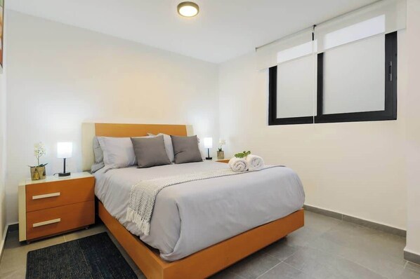 A modern bedroom with a bed, nightstands, and a window.