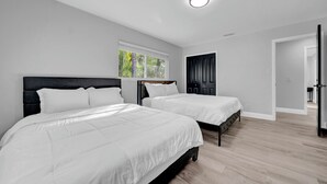 Un dormitorio moderno con dos camas, un ventanal grande y una puerta que da a otra habitación.