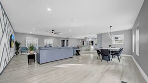 Amplia sala de estar con un sofá gris, una mesa de comedor con sillas y una cocina al fondo.