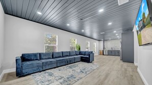 Amplia sala de estar con un sofá modular grande, un tapete estampado y una cocina al fondo.