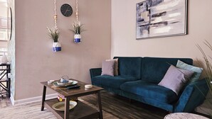 A living room with a blue sofa, a coffee table, a clock, and two hanging planters.