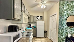 A compact kitchen with a microwave, toaster, stove, and refrigerator. A ceiling fan is visible above.