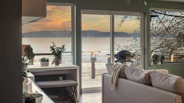 Een moderne woonkamer met een grote schuifpui naar een balkon met uitzicht op een meer.