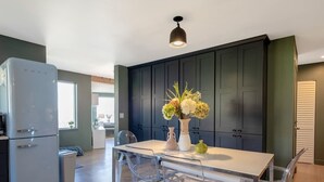 Eine moderne Küche mit einem weißen Kühlschrank, dunklen Schränken und einem Essbereich mit einem Glastisch und Stühlen.