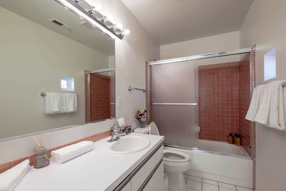 A bathroom with a white sink, mirror, and toilet. There is a shower area with a glass door.