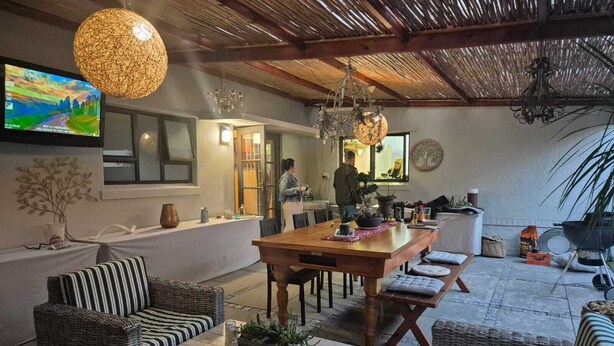 Un espacio al aire libre acogedor para comer, con muebles de mimbre, una mesa de madera y luces colgantes.