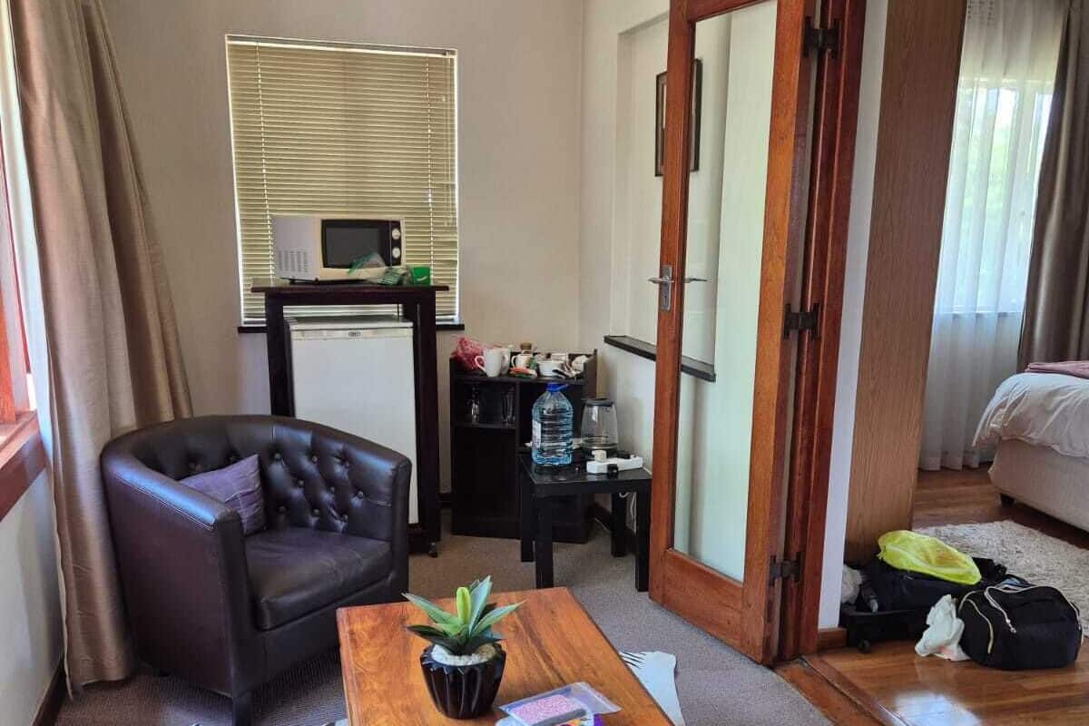 A hotel room with a leather armchair, a wooden table with a plant, a zebra-patterned rug, a minibar, and a bed with luggage.