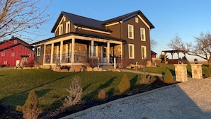 A two-story house with a porch, stone pillars, and a red barn in the background. - Rock Run Creek House (Goshen)