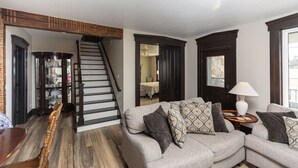 A living room with a grey sofa, patterned cushions, a wooden coffee table, a lamp, and a staircase leading to another room. - Rock Run Creek House (Goshen)