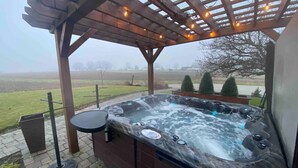 A hot tub under a wooden pergola with string lights, surrounded by a brick patio. - Rock Run Creek House (Goshen)