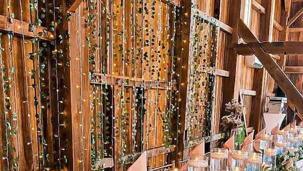 A long table with candles and greenery, set against a wooden backdrop with vertical strings of lights. - Rock Run Creek House (Goshen)