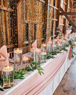 A long table with candles and greenery, set against a wooden backdrop with vertical strings of lights. - Rock Run Creek House (Goshen)