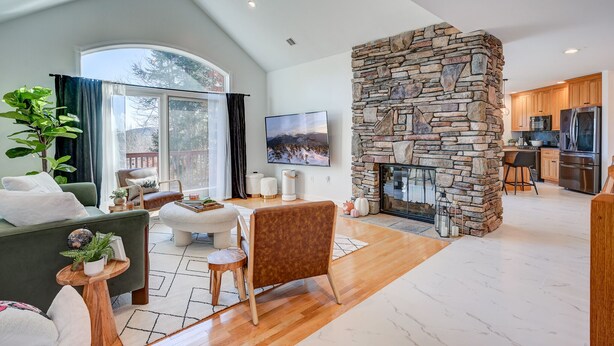 Amplia sala de estar con chimenea de piedra, un ventanal grande y una cocina moderna al fondo.