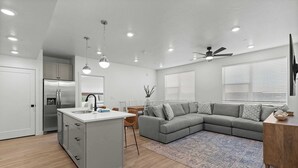 Een moderne keuken met een vast eiland, een grijze modulaire bank en een eethoek met een houten tafel en stoelen.