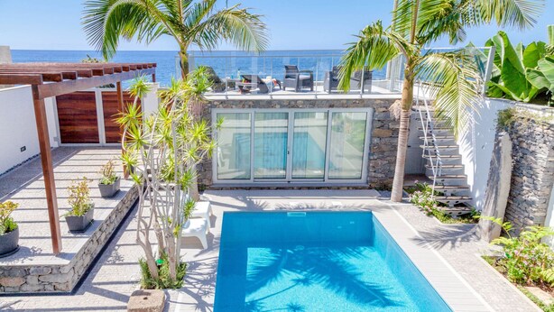 Ein Pool mit Meerblick, umgeben von Palmen und einer überdachten Sitzgelegenheit.
