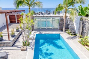 A swimming pool with a view of the sea, surrounded by palm trees and a covered seating area. - Madeira Beach House in Madalena do Mar (Ponta do Sol)