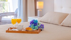 Ein ordentlich bezogenes Bett mit einem Frühstücksbrett, das Croissants und Saft sowie einen Blumenstrauß zeigt.