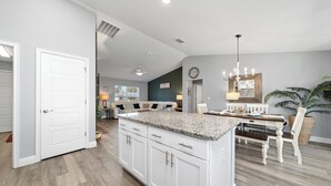 A spacious kitchen with a central island, white cabinetry, and a dining area with a wooden table and chairs. - Charming Cozy  3-bedroom house with WiFi, fitness room in lovely Ocala (Ocala)