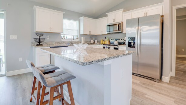 A modern kitchen with white cabinets, a large island, stainless steel appliances, and bar stools. - Charming Cozy  3-bedroom house with WiFi, fitness room in lovely Ocala (Ocala)