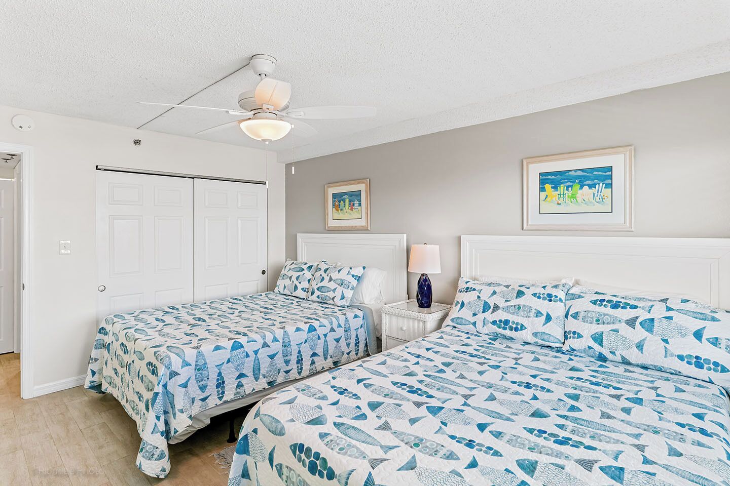 A bedroom with two beds, a ceiling fan, and two framed pictures on the wall.