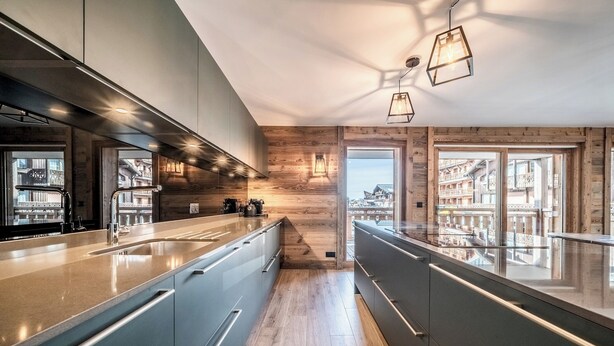 A modern kitchen with a long countertop, wooden accents, and a view of a building through the window.