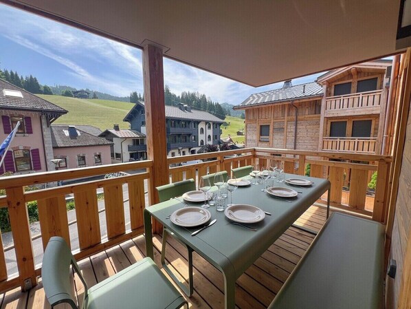 Une terrasse en bois avec une table dressée pour le repas, offrant une vue pittoresque sur un village.