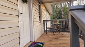 A wooden deck with a small table and chairs, a colorful mat, and a hanging plant.