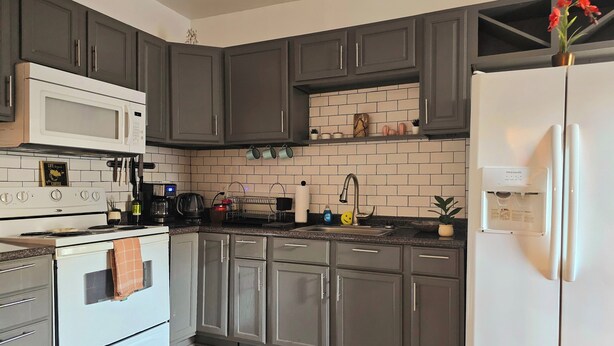 A modern kitchen with grey cabinets, a white refrigerator, a built-in microwave, and a coffee machine.