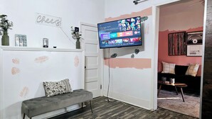 A room with a grey bench, a flat-screen TV mounted on the wall, and a door leading to another room.