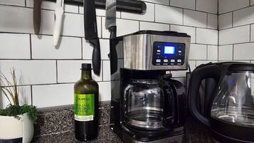 A kitchen with a coffee maker, a kettle, and a bottle of olive oil on the counter.