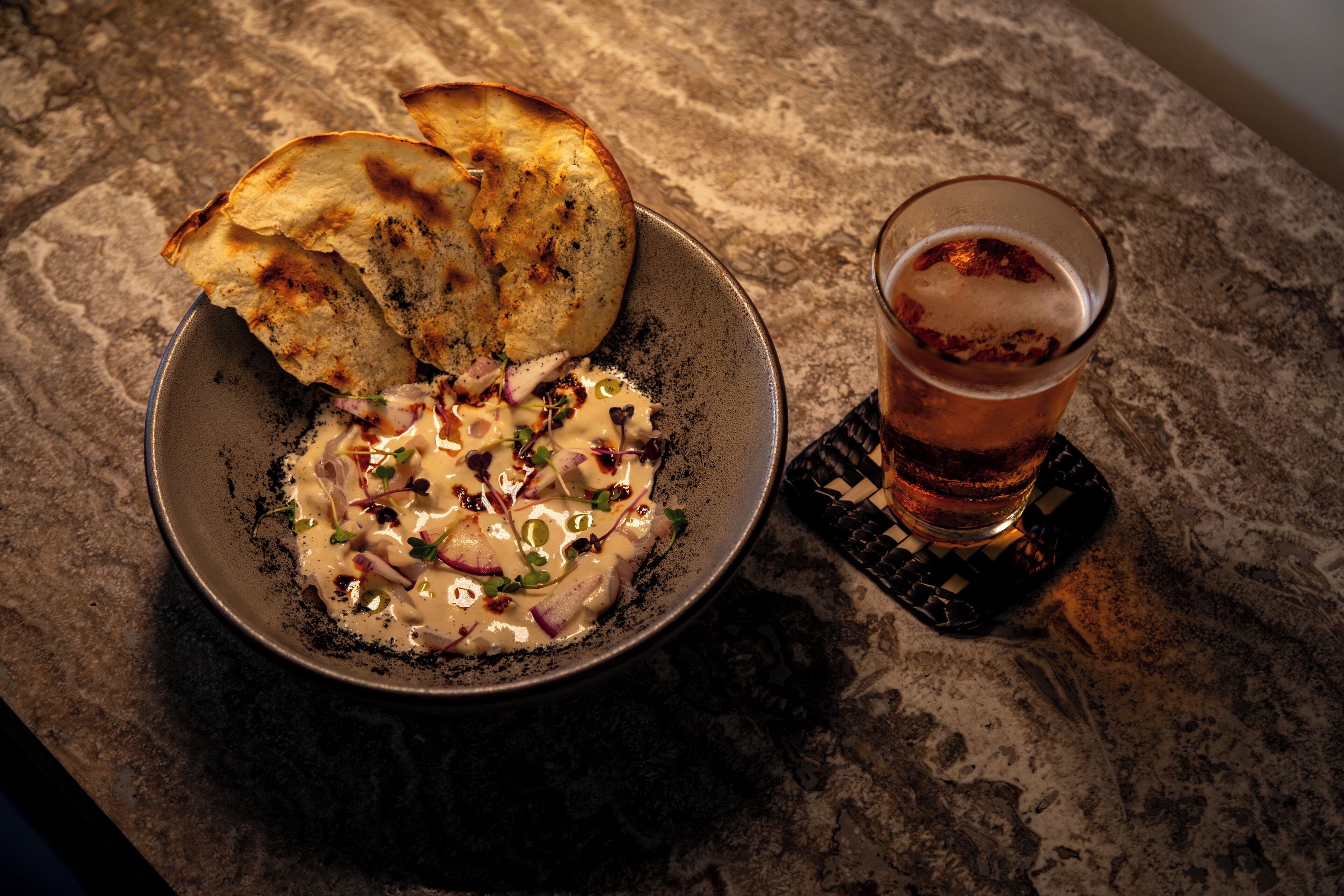 A bowl of food with bread and a glass of beer on a textured surface.