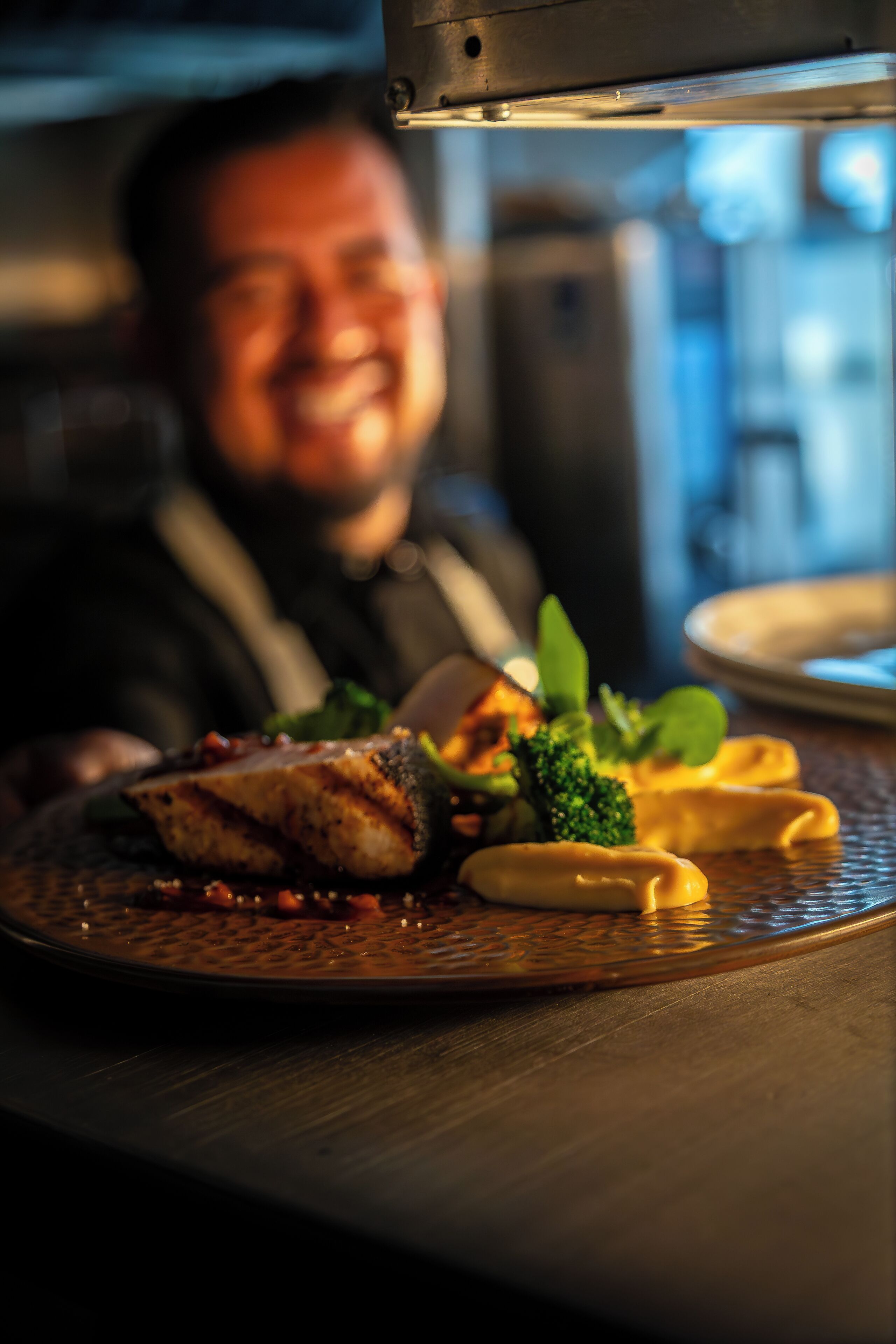 Un chef sonríe a un plato bien presentado sobre una mesa.