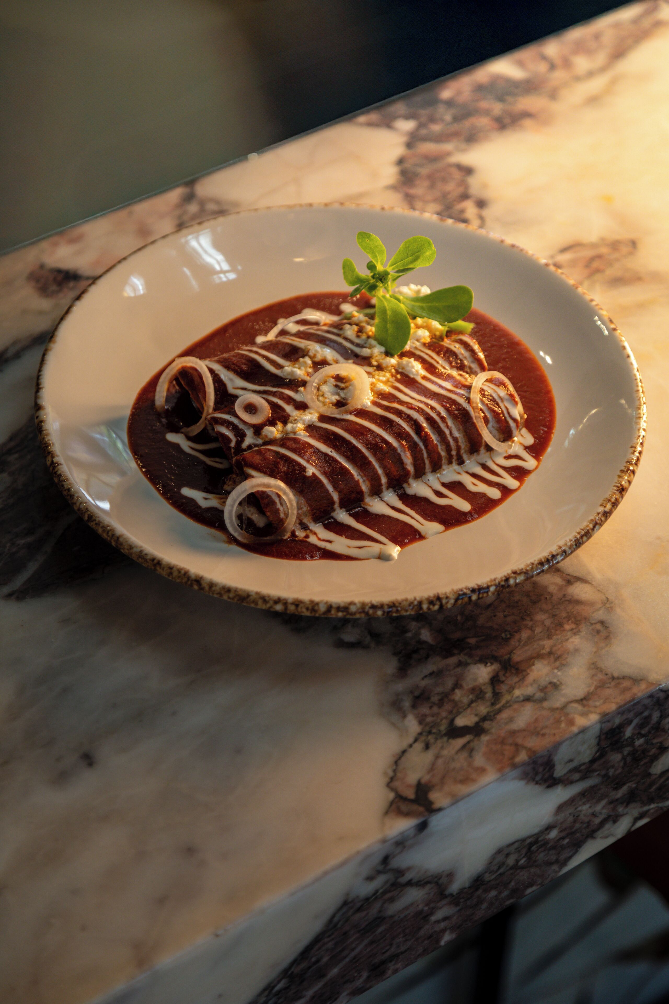 Une assiette d’enchiladas sur une table en marbre.
