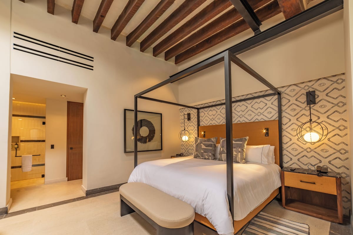 A modern bedroom with a four-poster bed, a wooden bench, and a nightstand with a lamp.