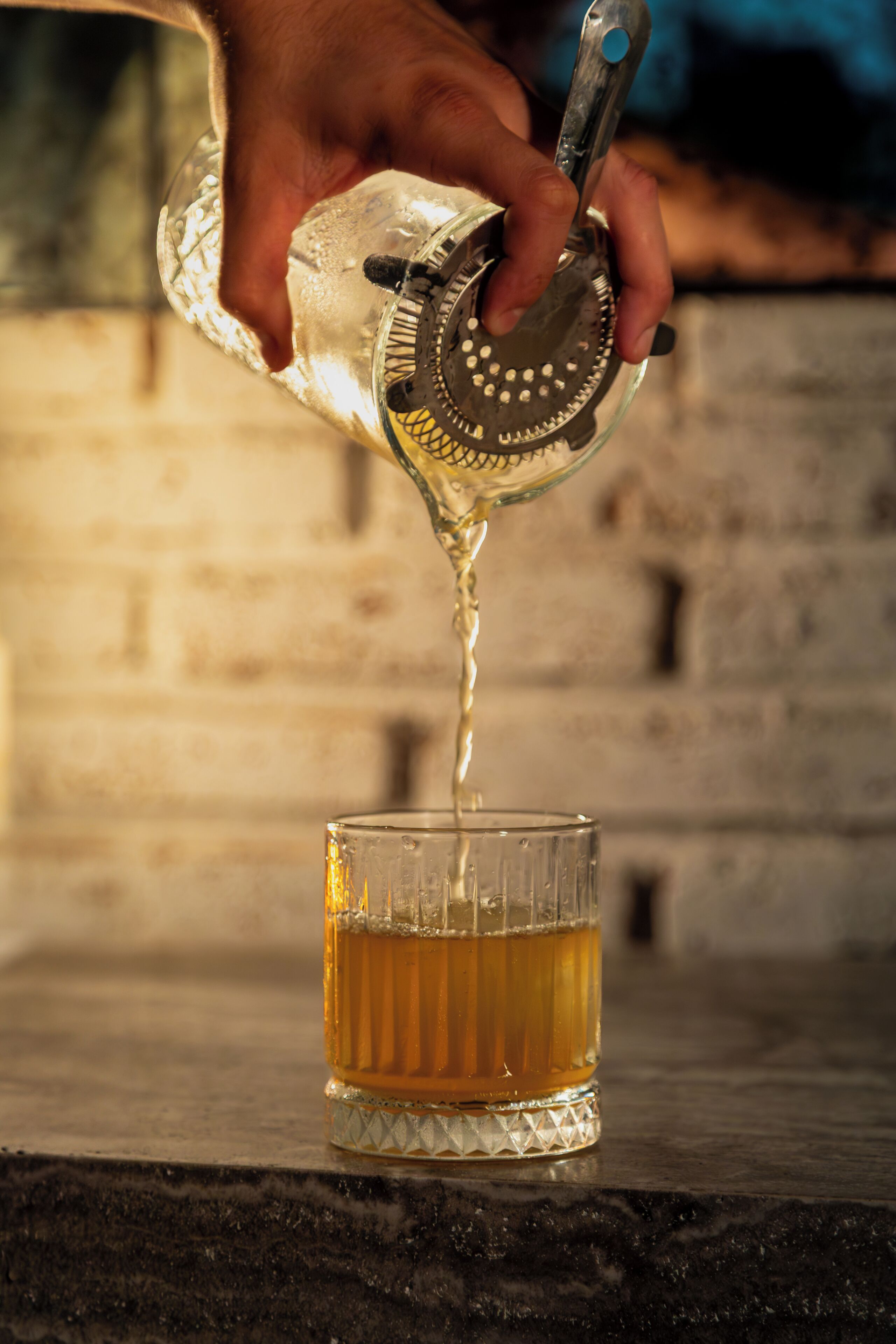 A hand pouring a liquid from a metal container into a glass.