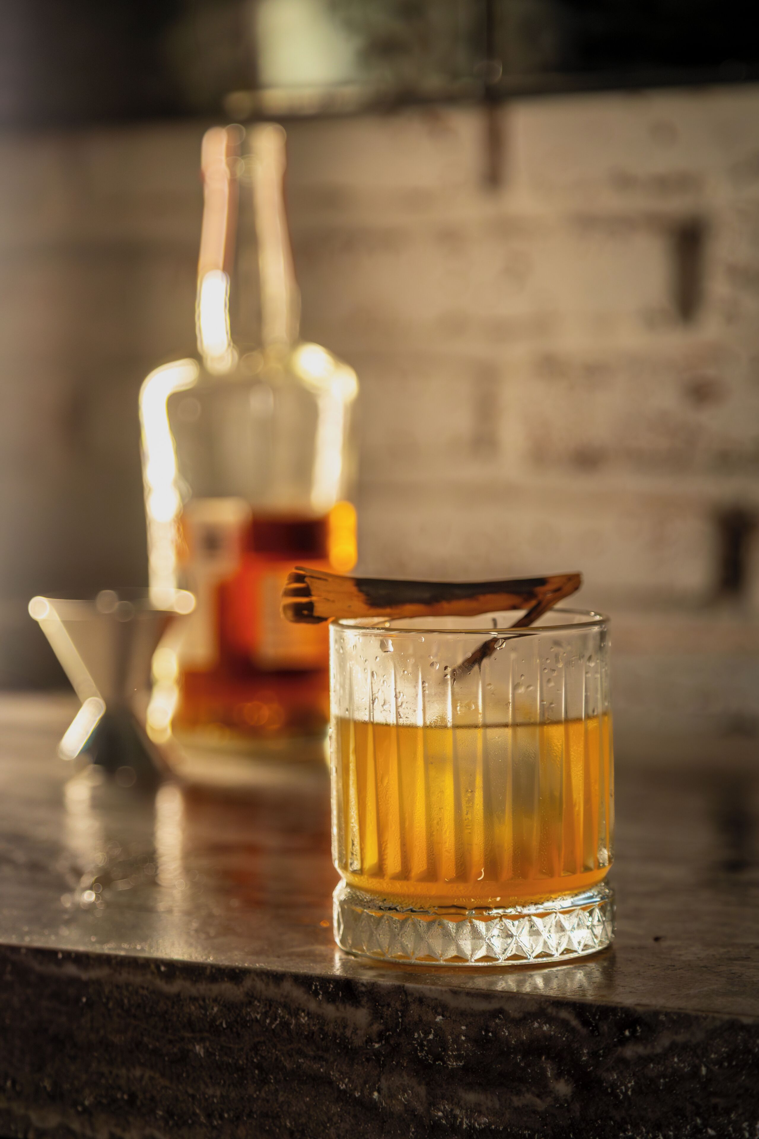 Un verre contenant un liquide ambré, posé sur un comptoir sombre, avec une bouteille floue en arrière-plan.