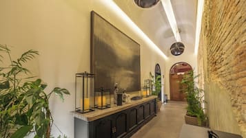 A hallway with a long reception desk, potted plants, and a large abstract painting on the wall.