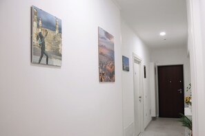 Ein Flur mit weißen Wänden, einer braunen Tür am Ende und drei gerahmten Kunstwerken.