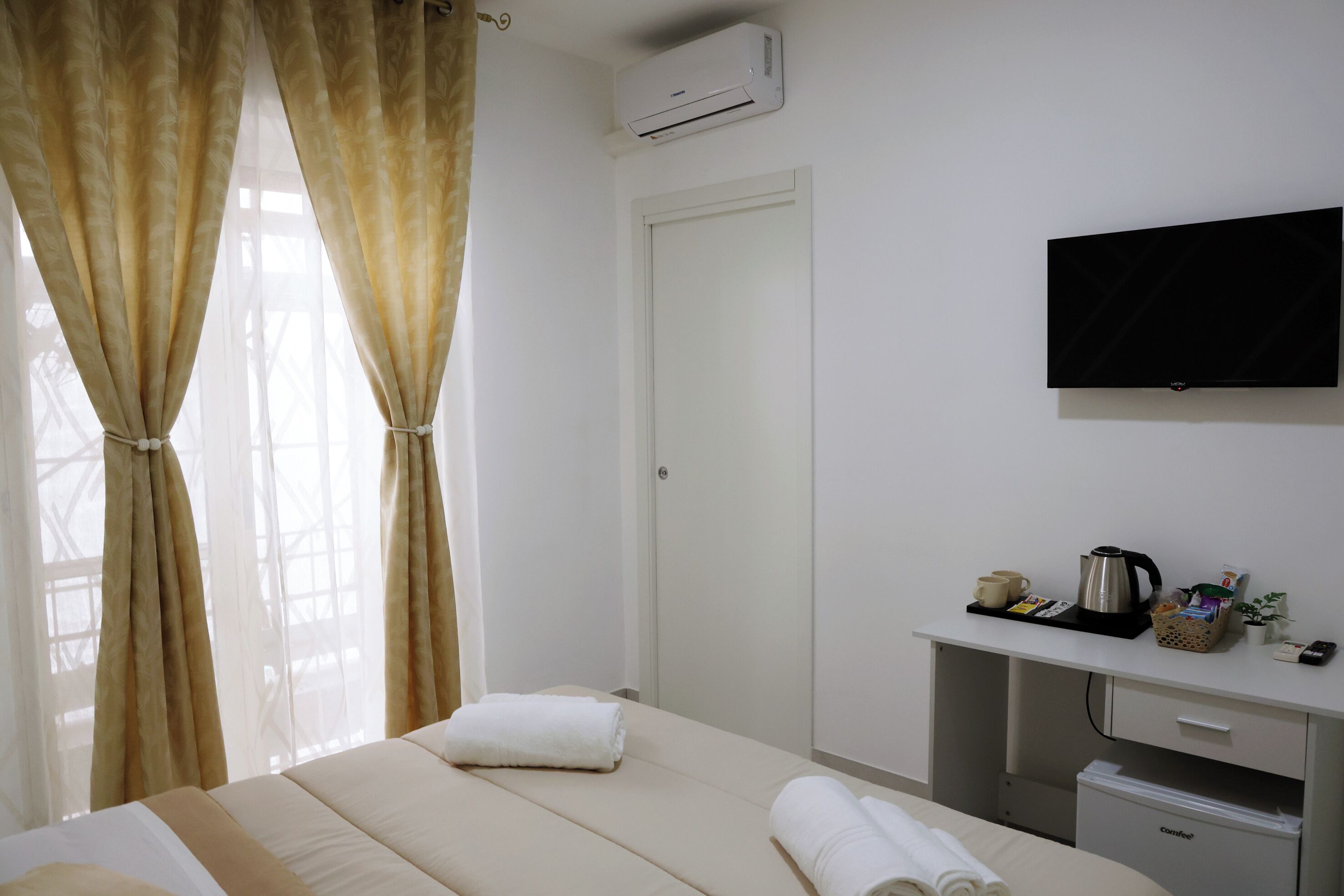 Une chambre d’hôtel équipée d’un lit, d’un téléviseur fixé au mur, d’un bureau avec une machine à café et d’un petit réfrigérateur.