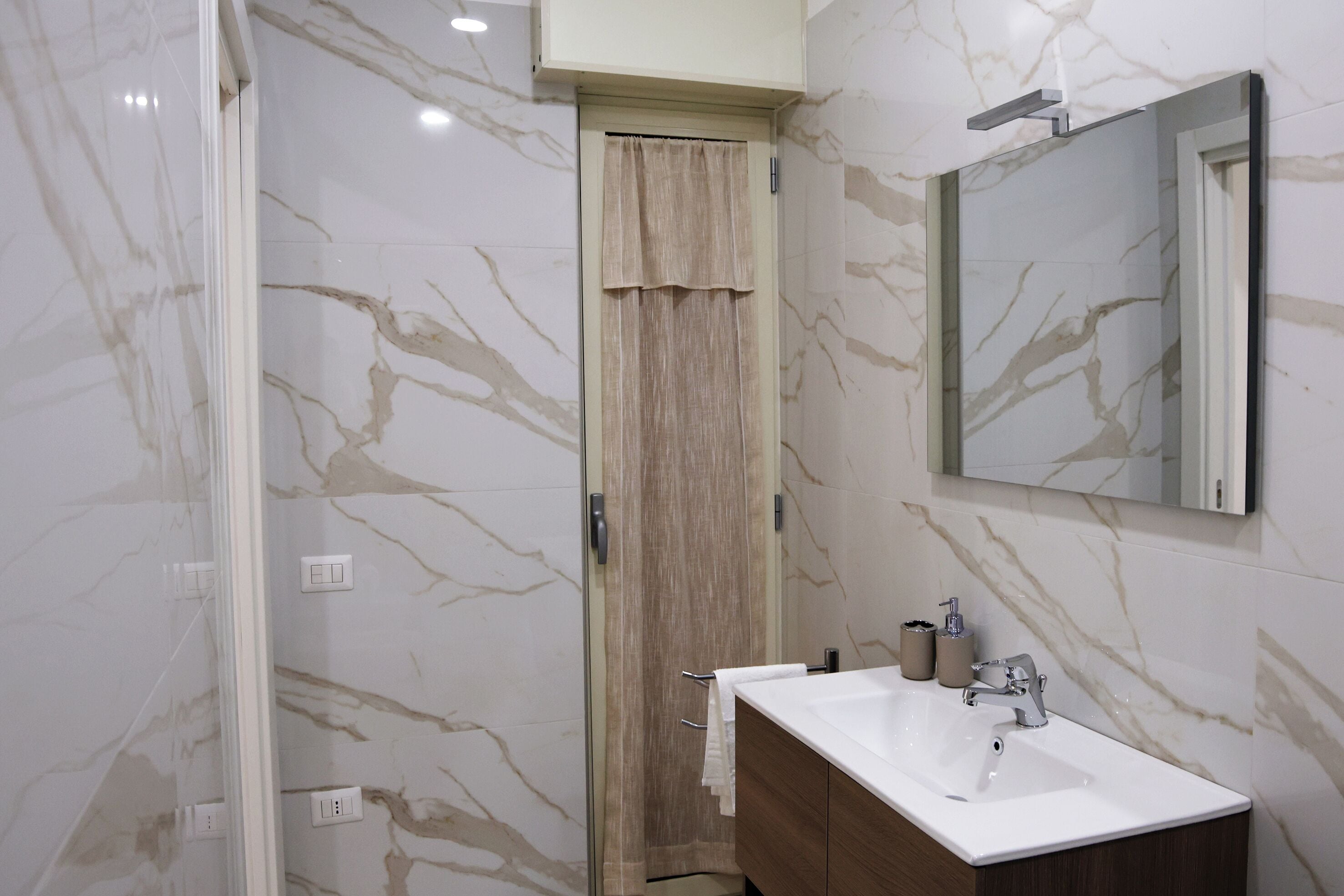 A modern bathroom with a marble backsplash, a wooden door, a white sink, and a mirror above it.