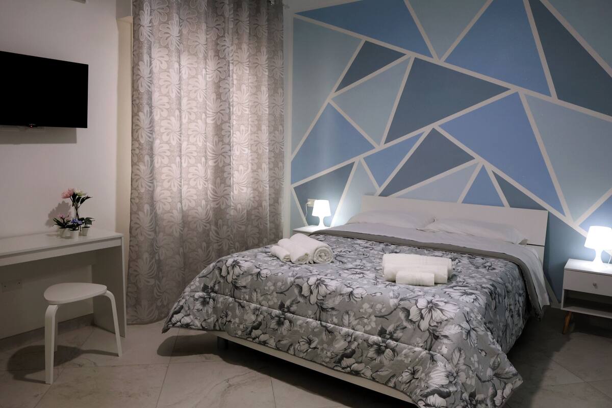Un dormitorio con cama, escritorio, silla, televisor y pared con diseño.