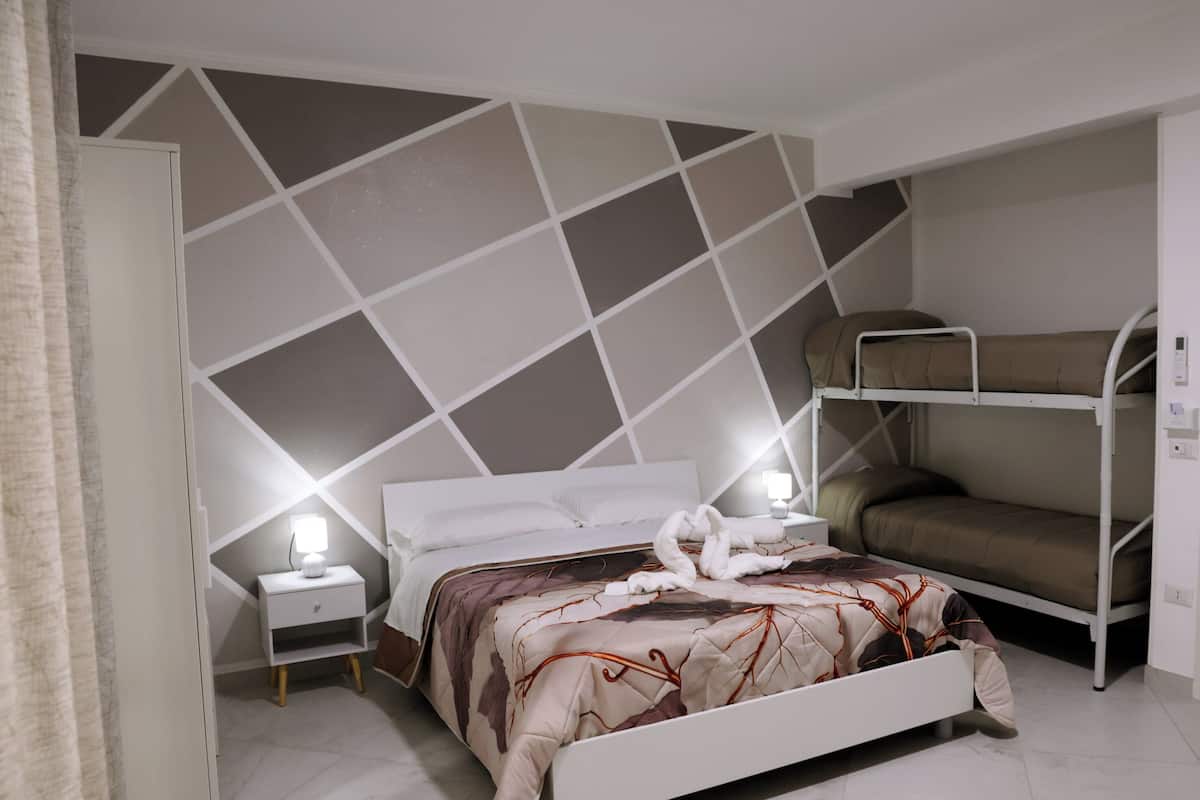 Una habitación de hotel con una cama, una mesita de noche, un aparador y una litera.