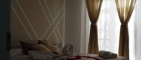 A hotel room with a neatly made bed, a decorative wall pattern, and a window with curtains.
