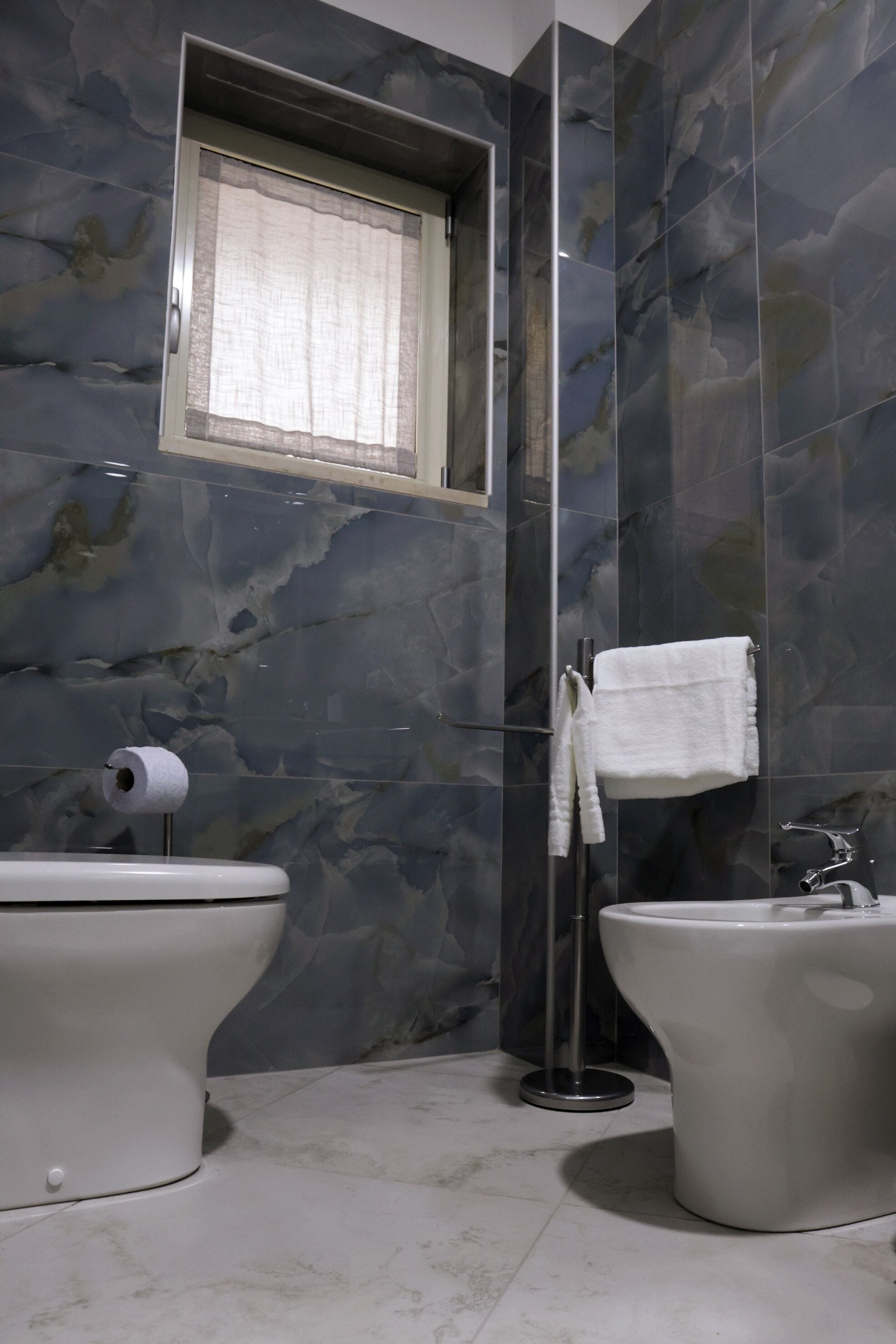 Un baño con dos lavamanos, un inodoro y una ventana con cortina.