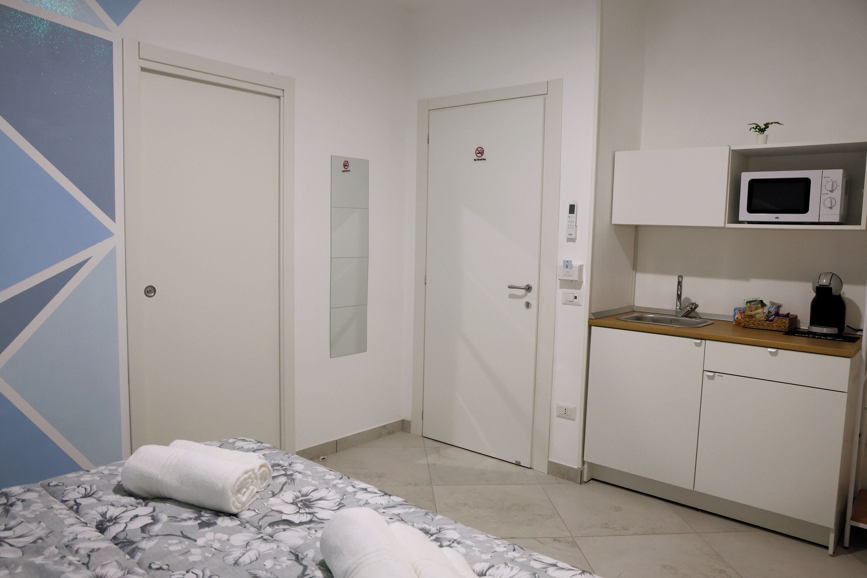 A hotel room with a bed, a bathroom, a kitchenette, and a door with a mirror.