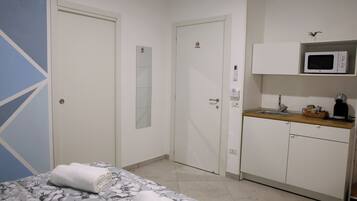A hotel room with a bed, a bathroom, a kitchenette, and a door with a mirror.