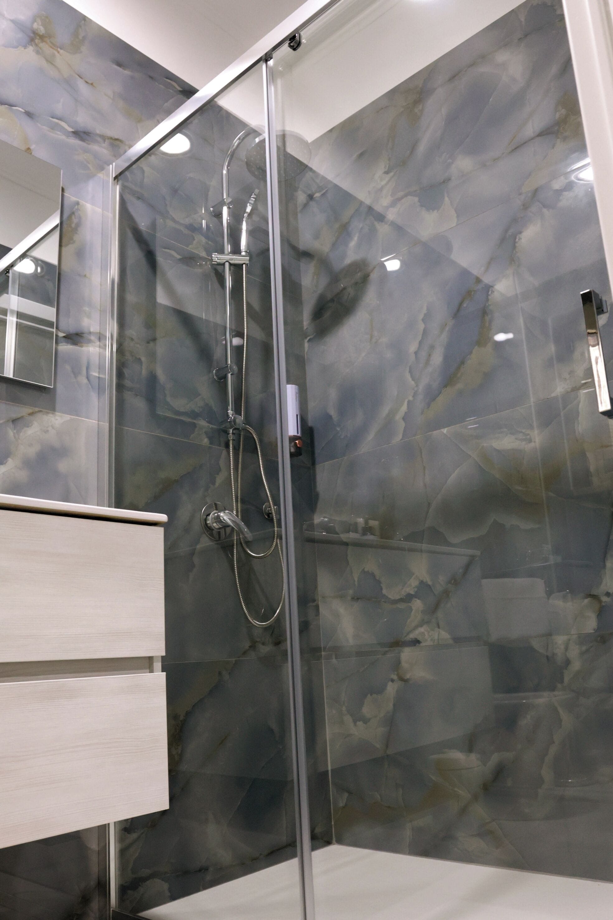 A modern bathroom with a glass-enclosed shower, marble walls, and a wooden vanity.