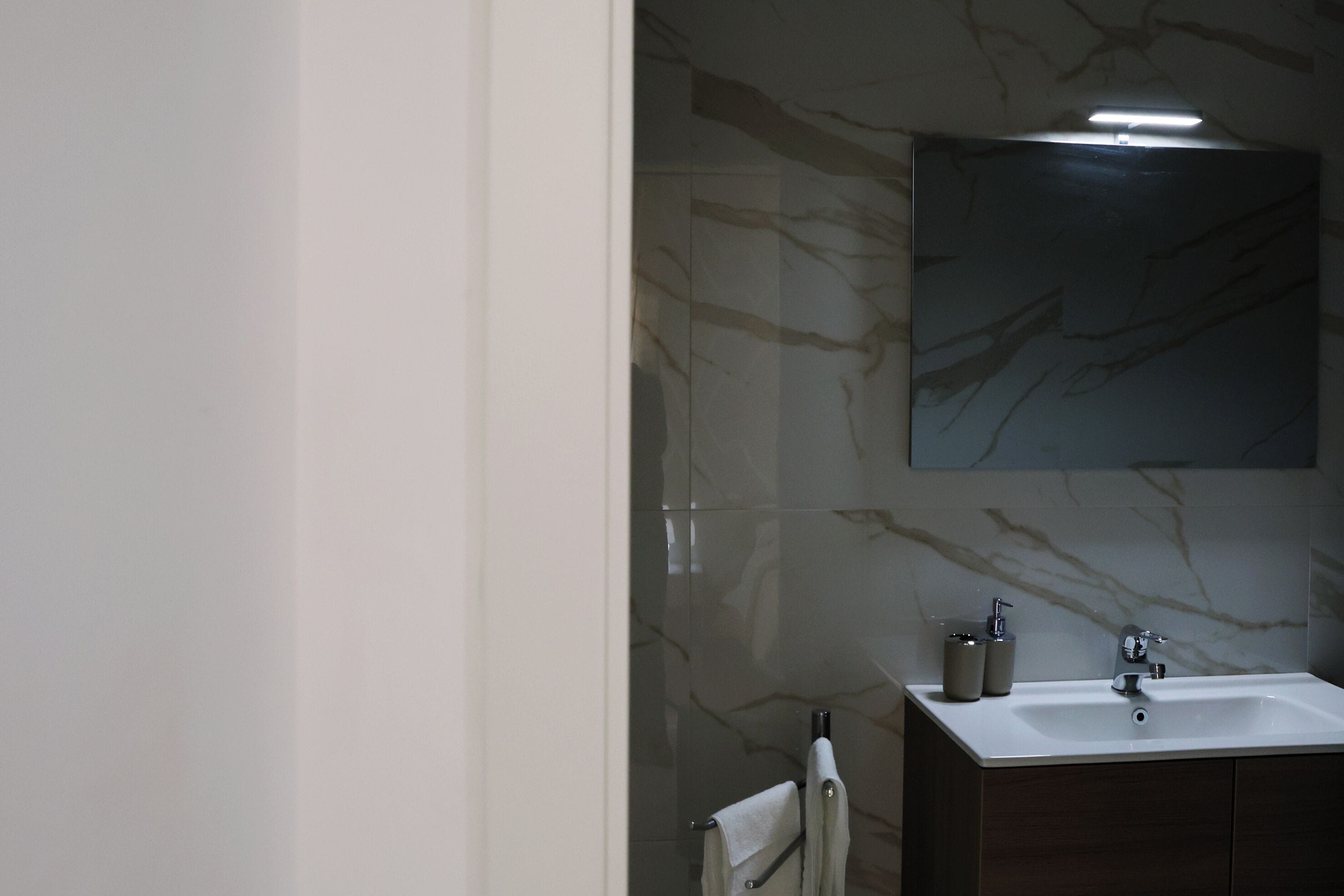 A bathroom with a marble wall, a sink, and a mirror.