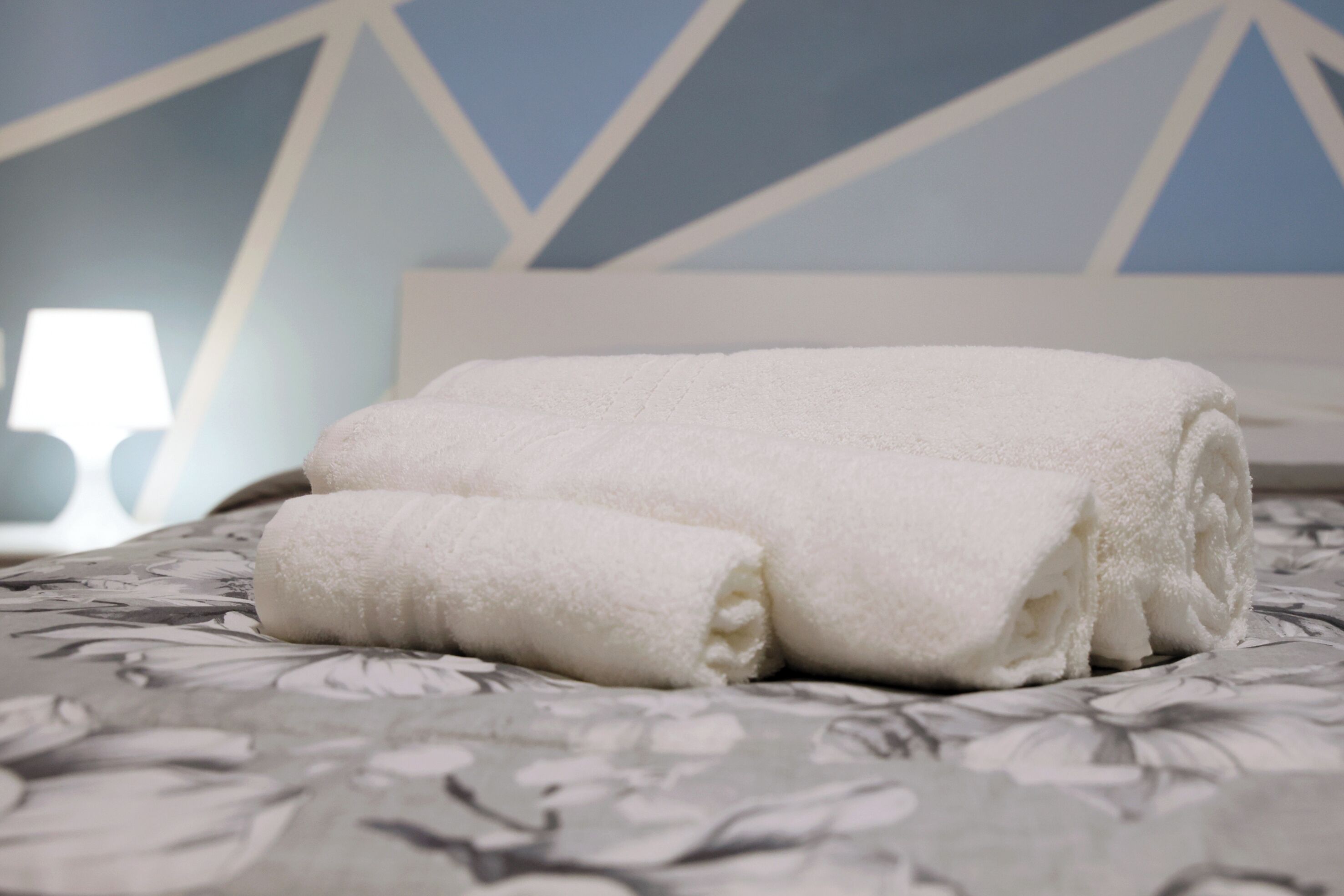 A neatly made bed with a floral-patterned bedspread and a rolled white towel.